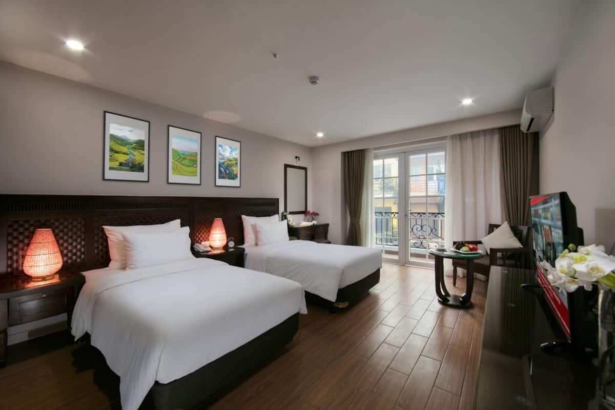 A hotel room with two beds, a desk, a TV, and a balcony with a view.