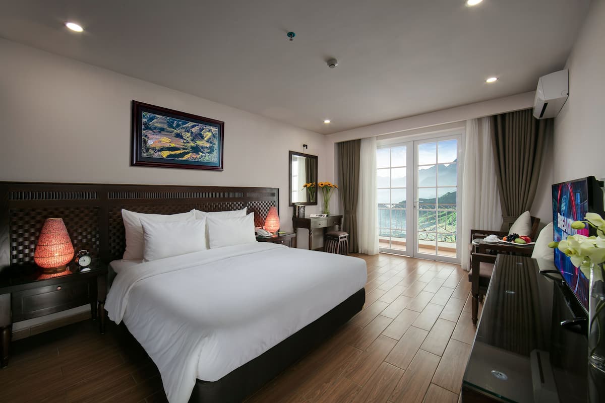 A hotel room with a large bed, a desk, a chair, a TV, and a window with a view.