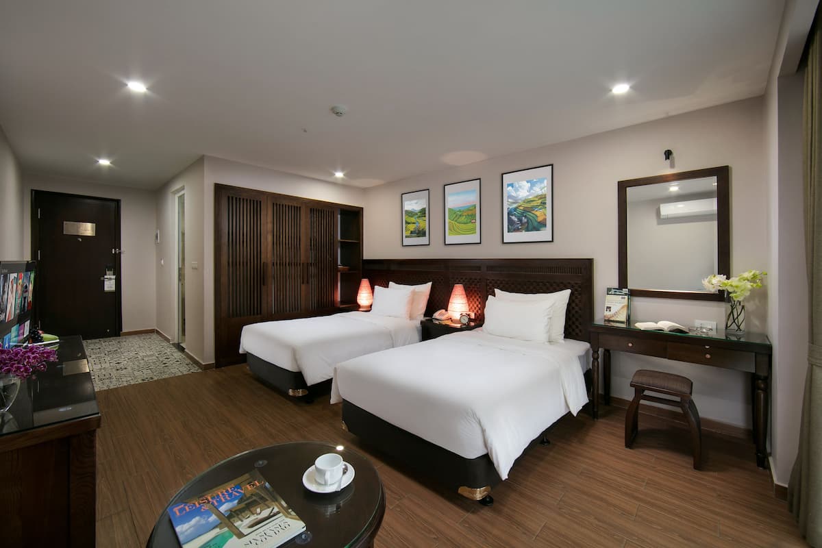 A hotel room with two beds, a desk, a chair, a coffee table, and a bookshelf.