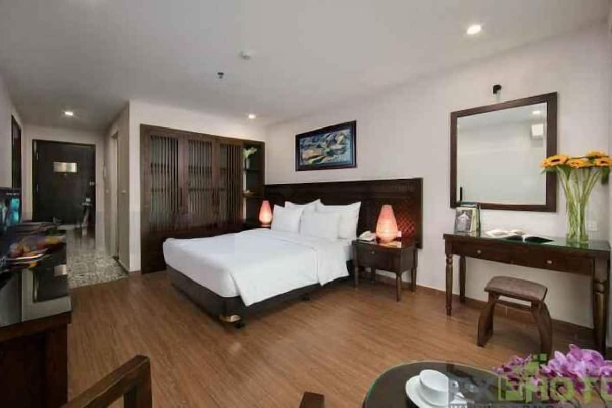 A hotel room with a bed, bedside table, lamp, desk, chair, and a mirror.