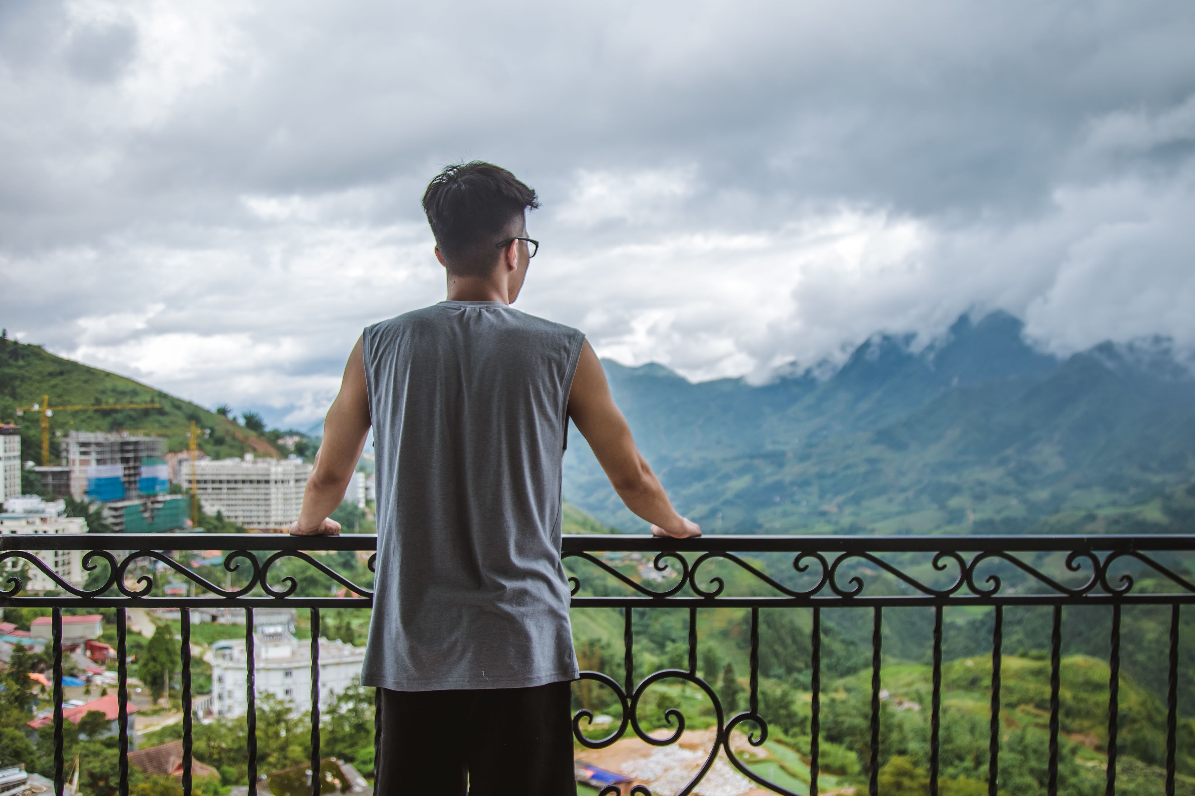 A person standing on a balcony overlooking a mountainous landscape with buildings in the background.