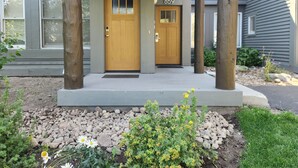 A two-story house with a porch supported by wooden posts, two doors labeled 858 and 859, and a landscaped front yard with rocks and plants.