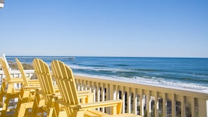 Blick auf einen Strand mit gelben Adirondack-Stühlen und einem Steg im Hintergrund.