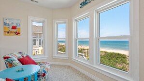Ein Zimmer mit großem Fenster zum Strandblick, ein farbenfroher Stuhl und ein kleiner Tisch.