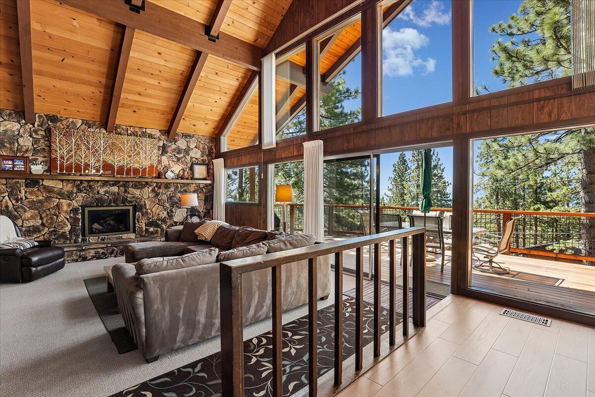 Un vaste espace de vie agrémenté d’une cheminée en pierre, de grandes fenêtres et d’un balcon donnant sur une forêt.