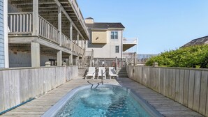 Une piscine dotée d’une terrasse en bois et de chaises longues, entourée de clôtures en bois et bordée d’un bâtiment avec des balcons.