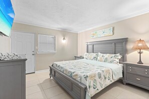 A bedroom with a bed, nightstands, a lamp, a door, and a window with blinds.