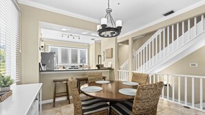 A dining area with a round table, wicker chairs, and a chandelier. - Cedars East #528 Townhome by RVA (Longboat Key)