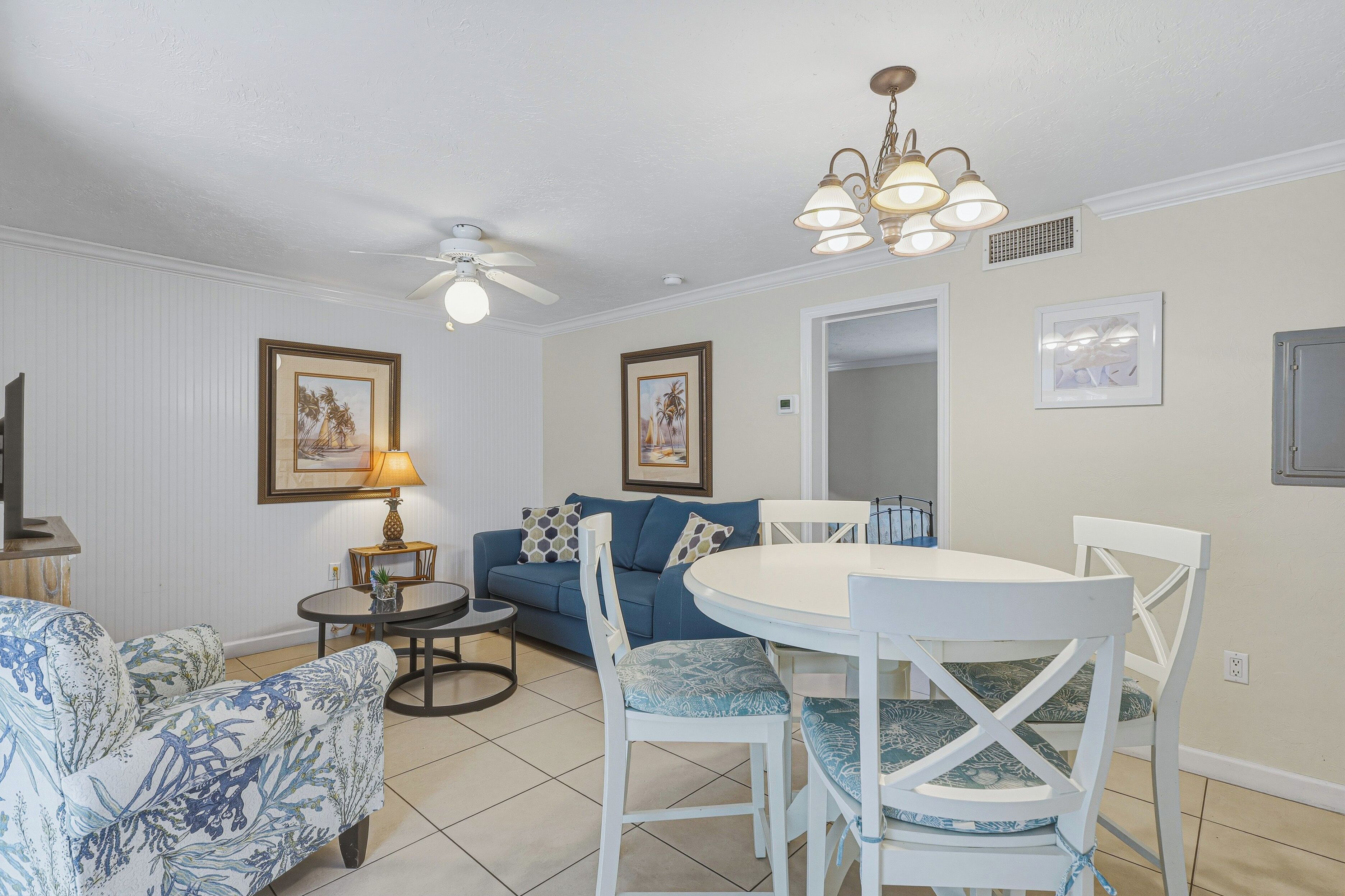 A living room with a sofa, a dining table with chairs, a ceiling fan, and wall-mounted artwork.