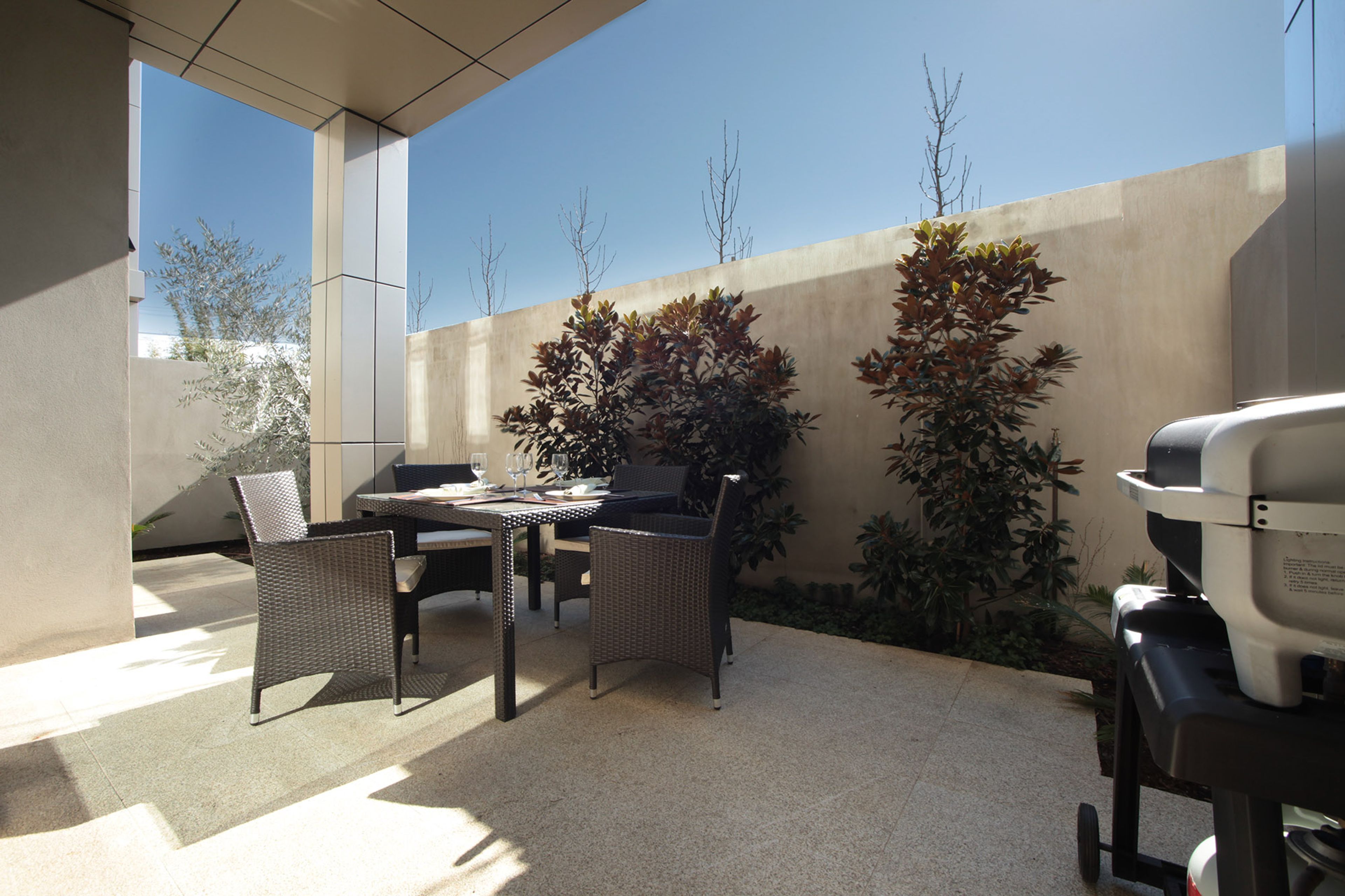 An outdoor patio area with a table and chairs, a barbecue grill, and potted plants.