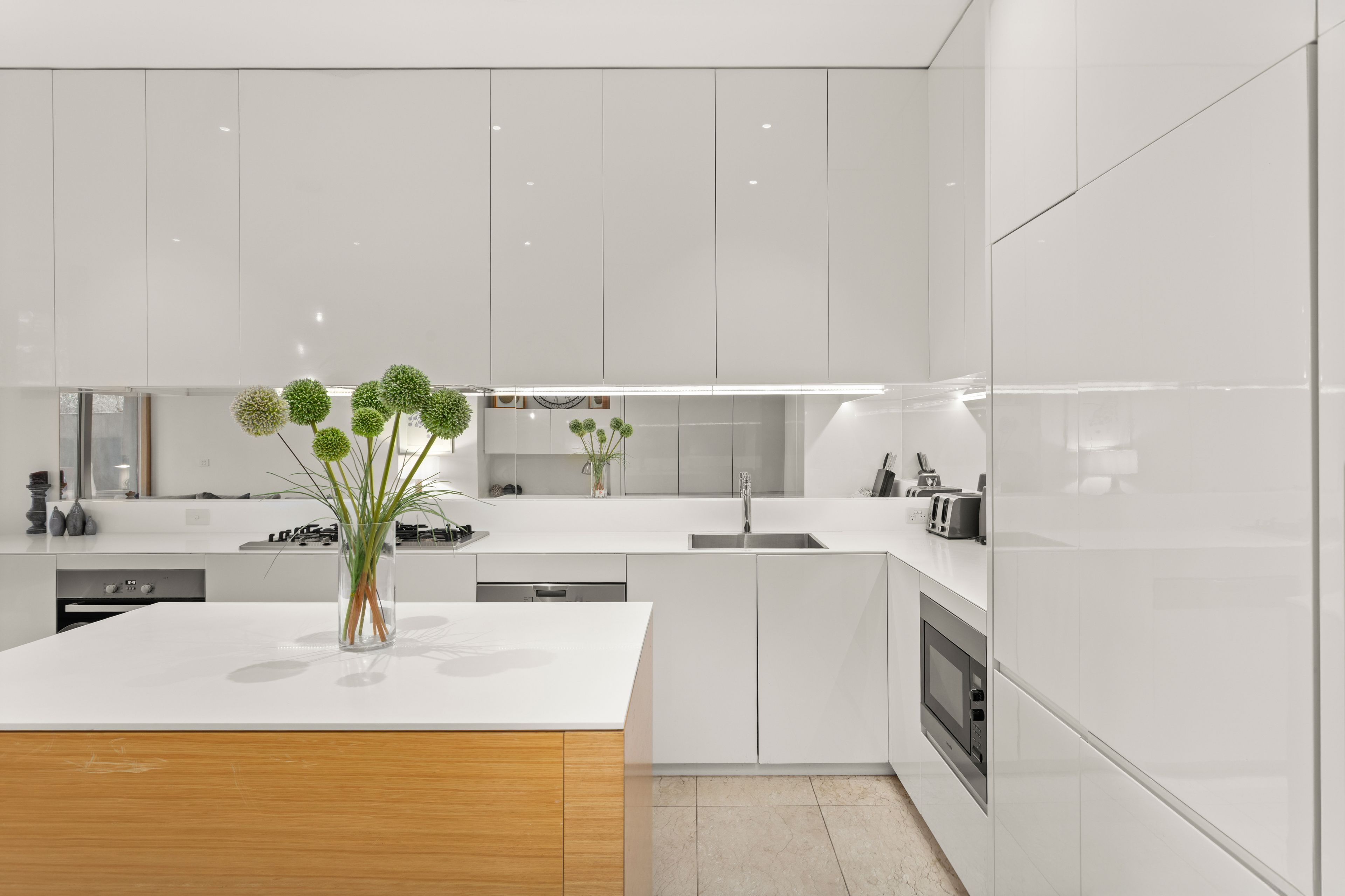 Une cuisine moderne avec des meubles blancs, un îlot central et un four encastré.