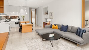 Ein zeitgemäßer Wohnraum mit Küche, Essbereich und einem grauen Sofa mit Kissen.