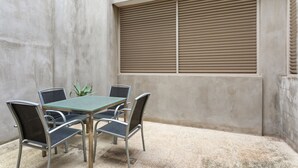 Eine Terrasse mit Tisch und Stühlen, ein Fenster mit Jalousien und eine Betonwand.