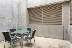 A patio area with a table and chairs, a window with blinds, and a concrete wall. - The Residence Pet Friendly Retreat Dendy Victoria (Brighton)