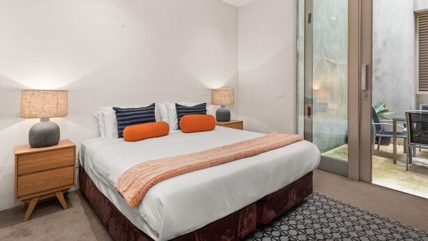 Ein modernes Schlafzimmer mit einem großen Bett, zwei Nachttischen und einer Schiebeglastür, die auf einen Balkon führt.