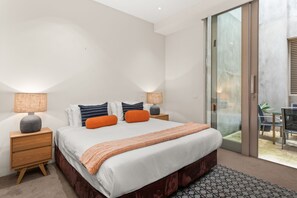 A modern bedroom with a large bed, two bedside tables, and a sliding glass door leading to a balcony. - The Residence Pet Friendly Retreat Dendy Victoria (Brighton)