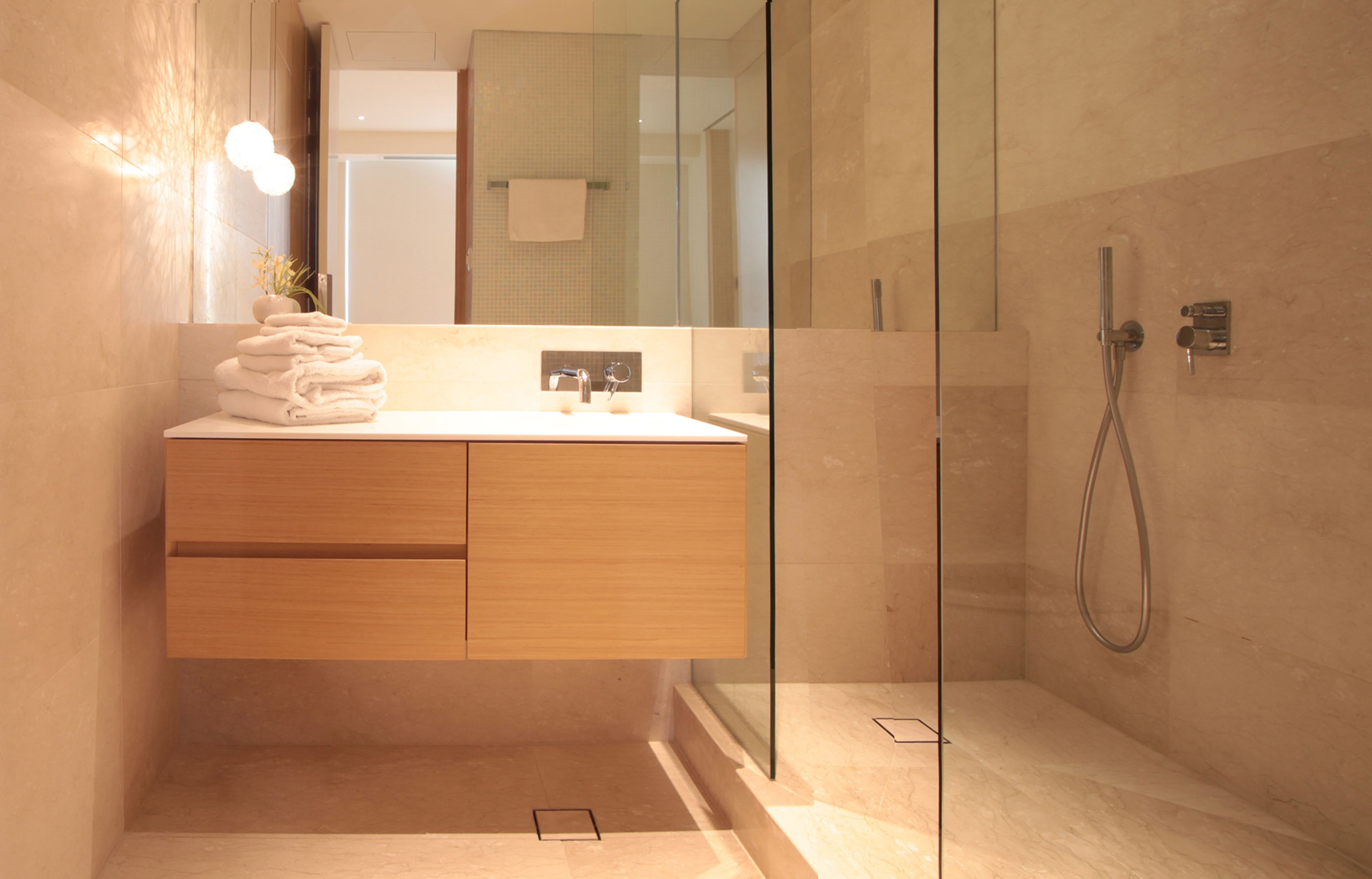 A modern bathroom with a glass-enclosed shower, a wooden vanity, and a stack of white towels.