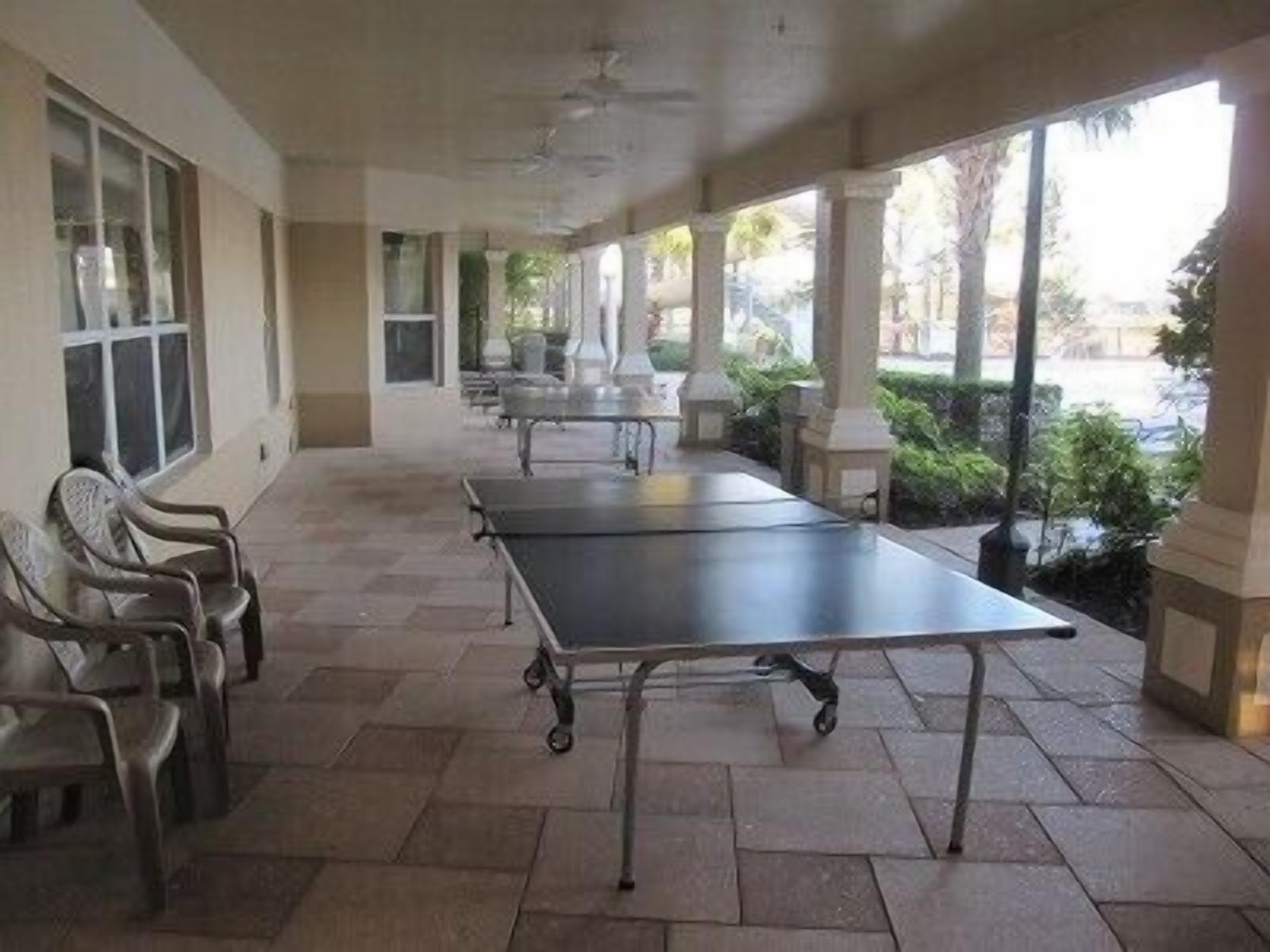 A covered outdoor area with a ping pong table, chairs, and a view of the street.