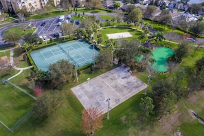 Une vue aérienne d’un complexe sportif comprenant plusieurs courts de tennis, entouré de verdure et de bâtiments résidentiels.