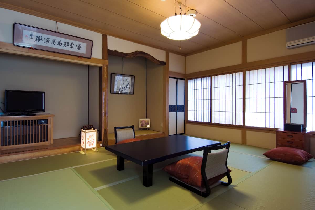 A traditional Japanese room with tatami flooring, a low table, a television, and a shoji screen.