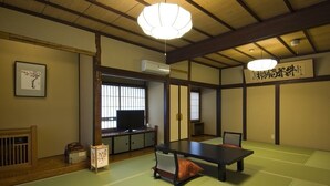 Una habitación japonesa tradicional con suelo de tatami, una mesa baja, un cojín, un televisor y una puerta corredera.