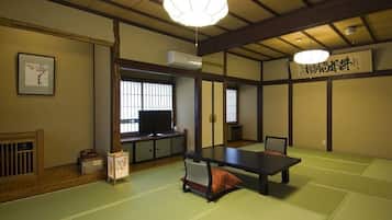 Um quarto japonês tradicional com tatames, uma mesa baixa, um assento almofadado, uma televisão e uma porta deslizante.