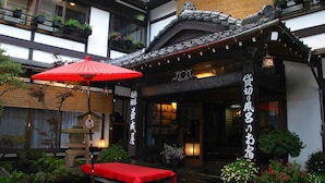 Un edificio japonés tradicional con un paraguas rojo, un farol de piedra y un pequeño jardín con una banca.