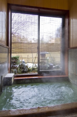 A hot spring bath with a view of a garden through a sliding door.