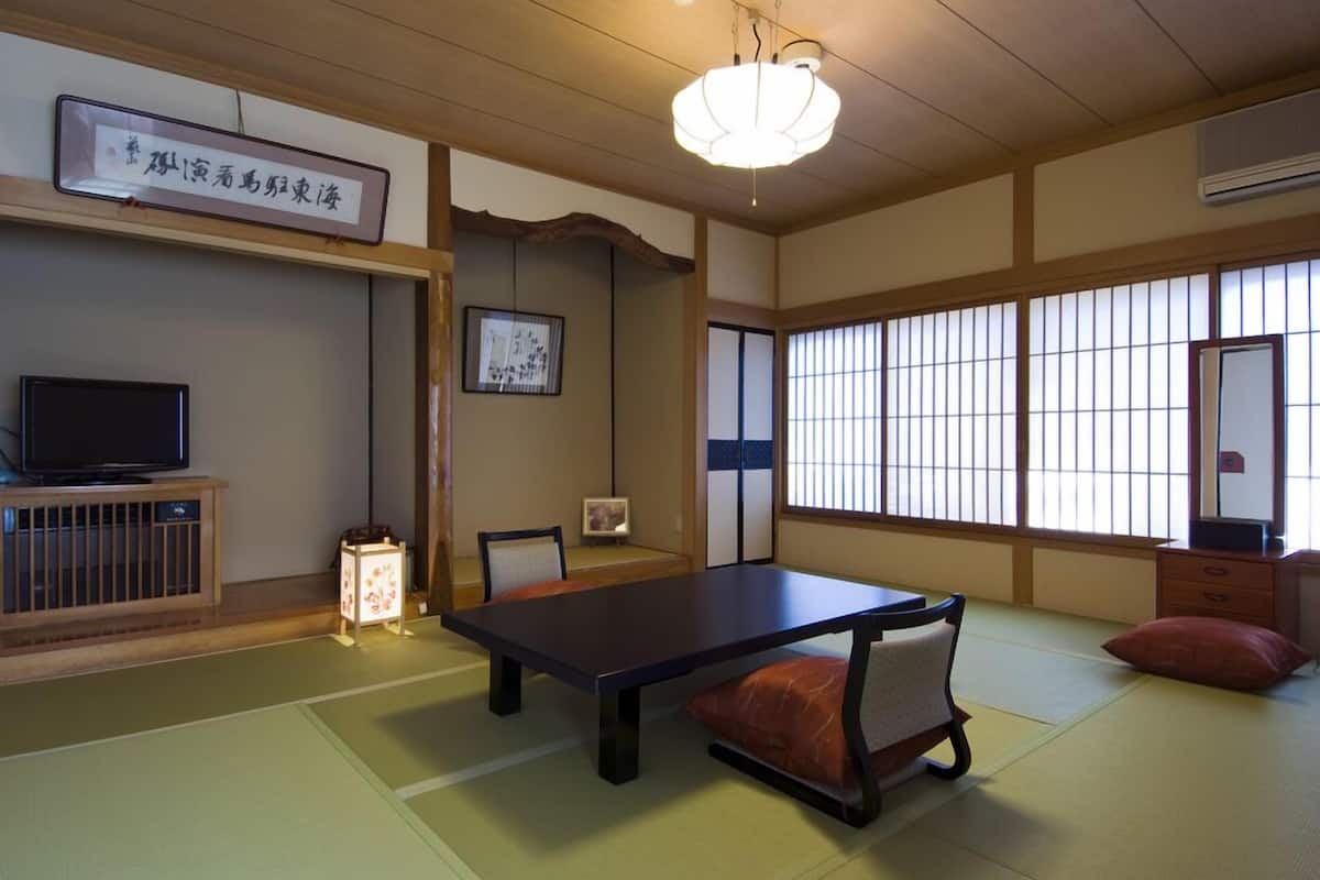 A traditional Japanese room with tatami flooring, a low table, a television on a wooden stand, and sliding shoji doors.