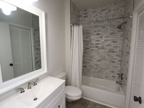 Une salle de bain avec un lavabo blanc, deux robinets, des toilettes et une baignoire avec un rideau de douche.