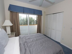 Une chambre à coucher avec un lit, une table de chevet, une lampe, une fenêtre avec des rideaux et un placard.