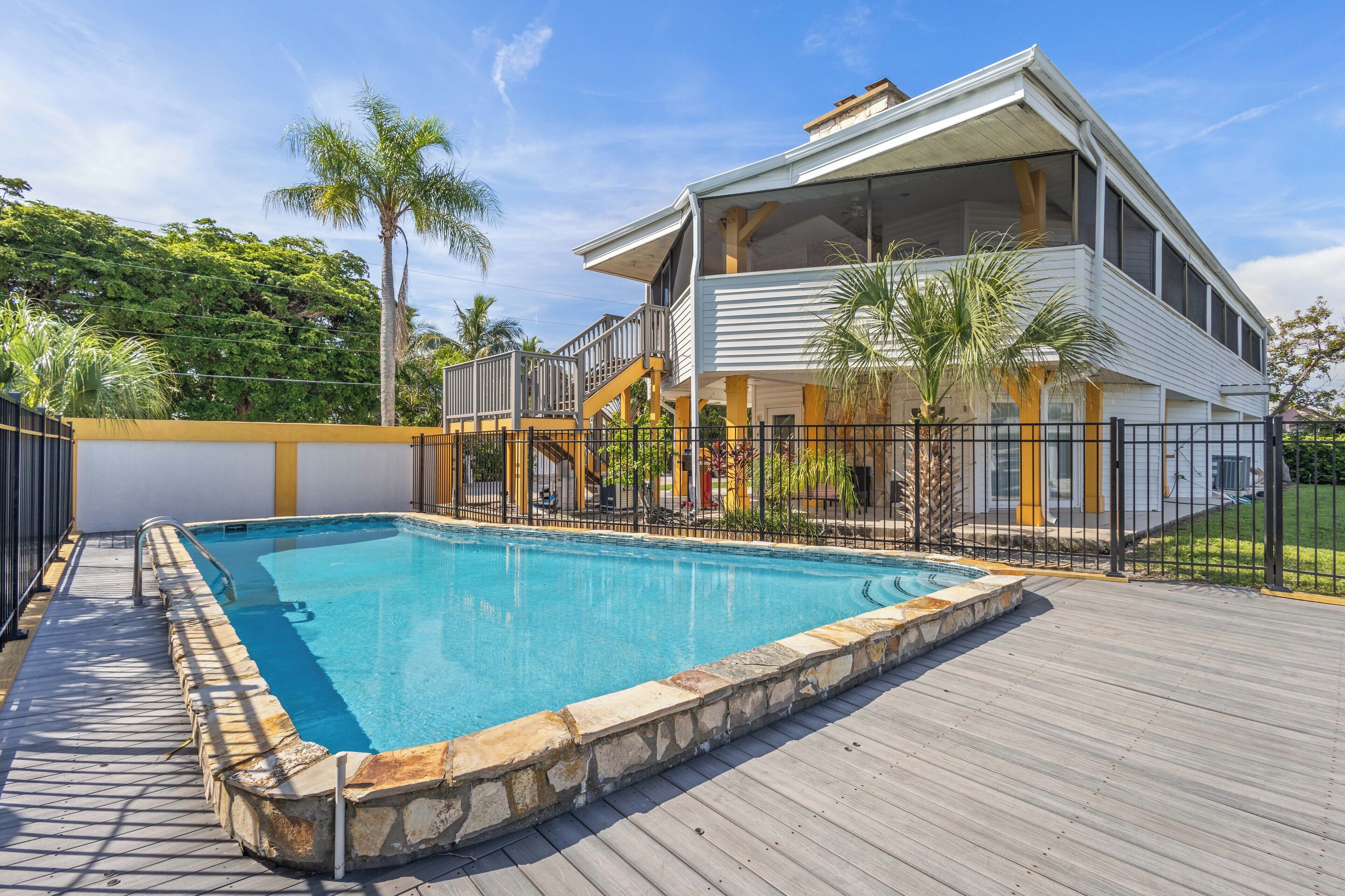 Una casa de dos pisos con piscina, un muelle de madera y un patio cercado.