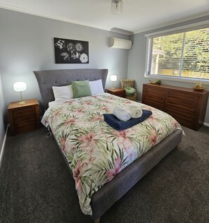 Um quarto com cama, mesas de cabeceira, cômoda, janela com persianas e ar-condicionado fixado na parede.