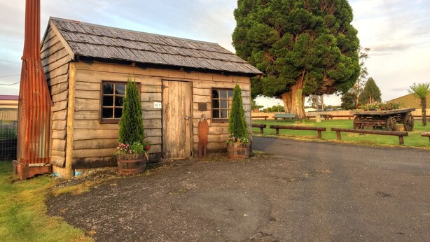 Un rustico chalet in legno con un camino, un albero grande e un piccolo carretto.