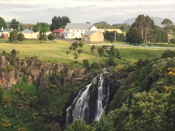 A waterfall cascading down a rocky cliff surrounded by lush greenery and a few buildings in the background.