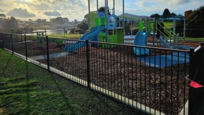 Un'area giochi con scivoli e strutture per arrampicarsi, circondata da una recinzione e un prato.