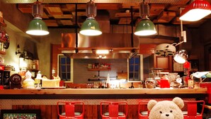 Una zona de bar con sillas rojas, un gran osito de peluche y varios utensilios de cocina sobre la encimera.
