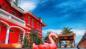 Un edificio rojo con piscina y un flamenco inflable gigante.