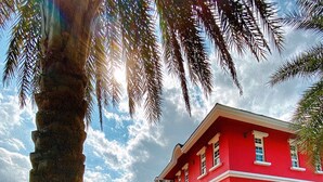 Un edificio rojo con un patio empedrado, rodeado de follaje y palmeras.