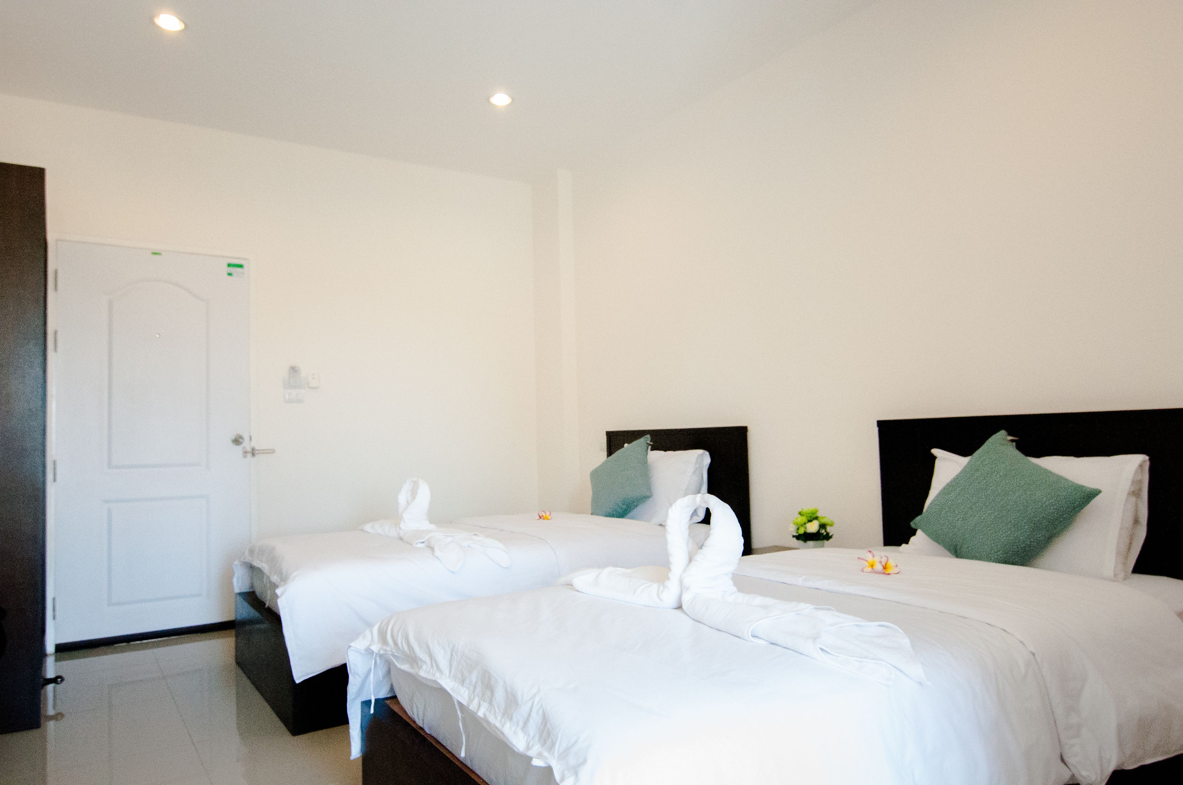Une chambre d’hôtel avec deux lits, du linge de lit blanc et des oreillers verts.