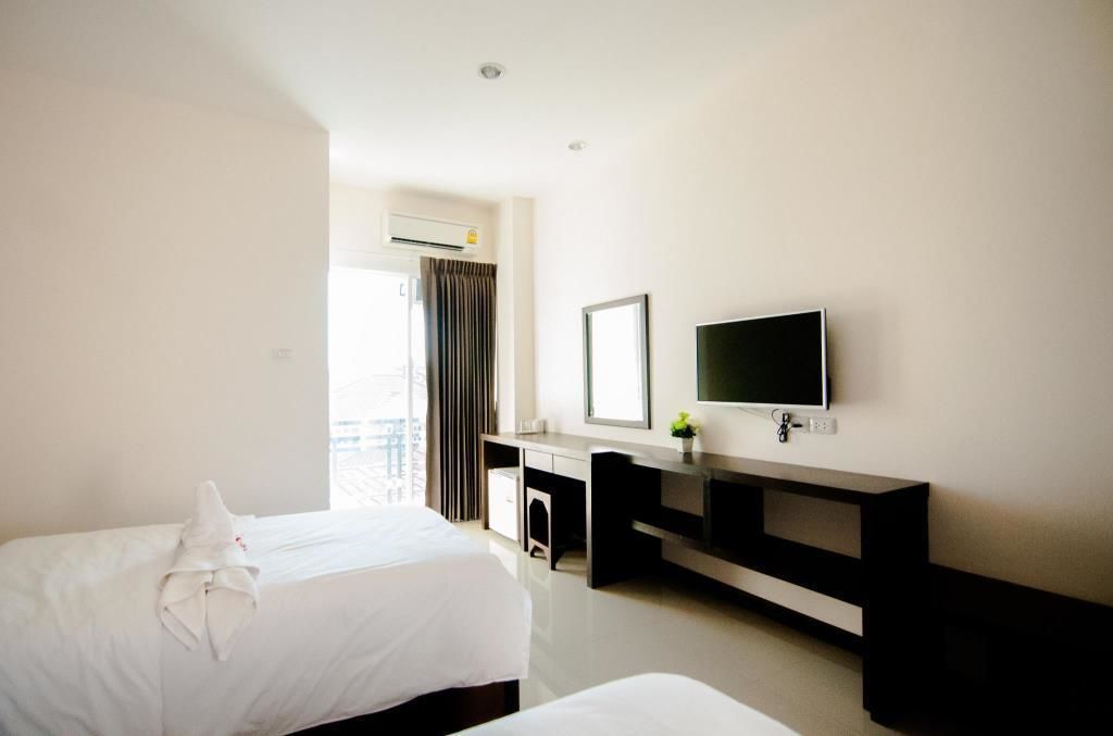 A hotel room with two beds, a desk, a TV, and an air conditioning unit.