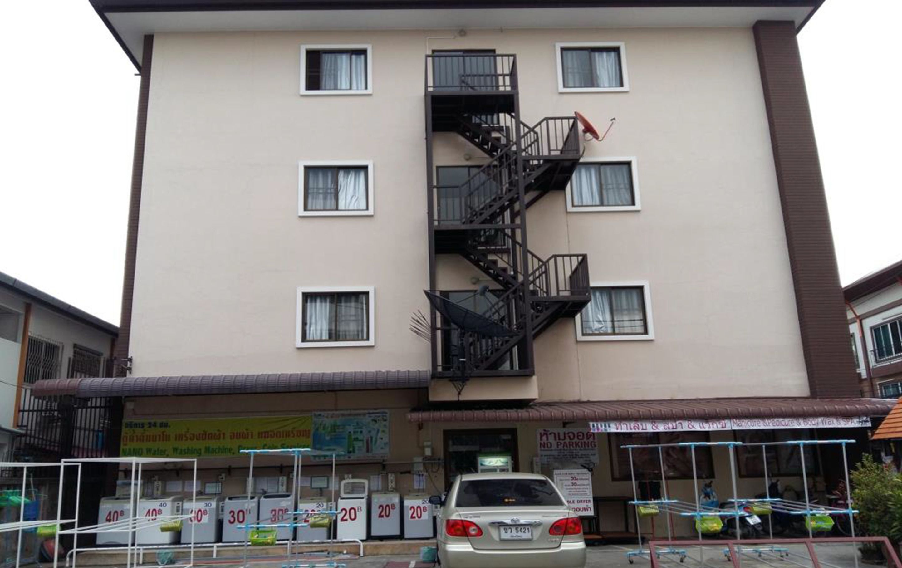 Un edificio de varios pisos con una escalera central, varias ventanas y un cartel que indica zona de prohibido estacionar.