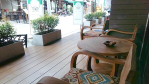 Un espace extérieur aménagé avec des tables et des chaises en bois, des plantes en pot et une vue sur la rue.