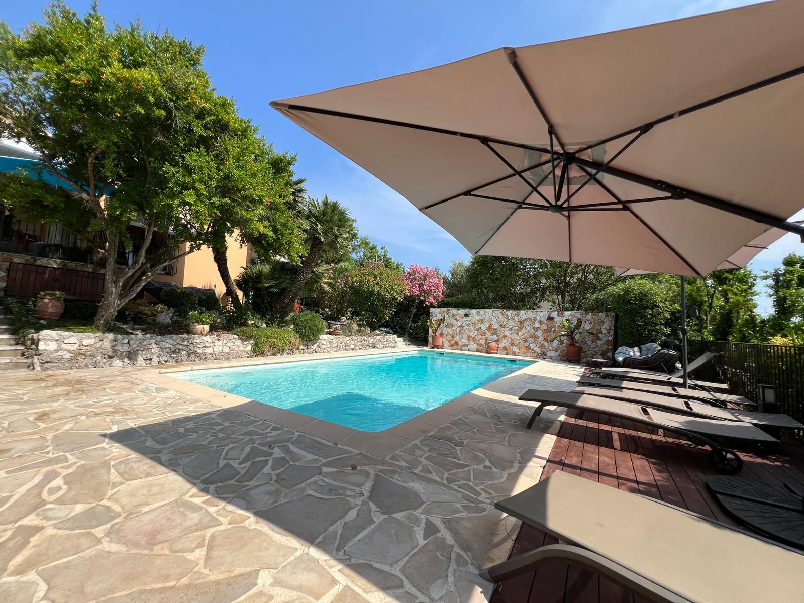 Una piscina con piastrelle in pietra, circondata da un patio con mobili da esterno e un ombrellone grande.