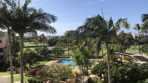 A pool area surrounded by palm trees and a golf course, with a clear view of the ocean in the background. - Ocean & golf views , watch amazing sunsets over Lana'i- J301 2/2 Sleep up to 7 (Lahaina)