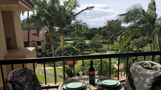 A balcony with a table, two chairs, and a bottle of wine. - Ocean & golf views , watch amazing sunsets over Lana'i- J301 2/2 Sleep up to 7 (Lahaina)
