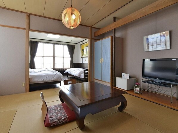 A traditional Japanese-style room with tatami flooring, a low table, two beds, a television, and a sliding door. - Yumoto Miyoshi (Beppu)