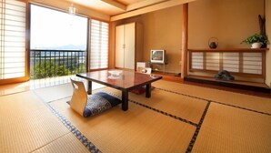 Una habitación japonesa tradicional con suelo de tatami, una mesa baja, un televisor y vistas a la ciudad.