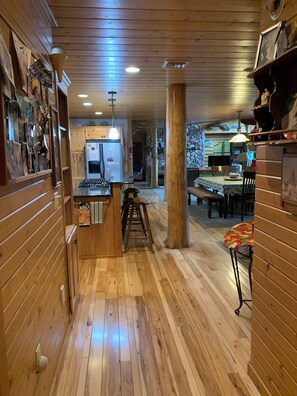 A wooden interior with a kitchen, dining area, and a stone wall.