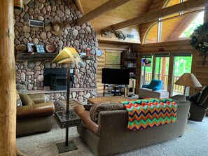 A log cabin interior with a stone fireplace, leather furniture, and a television.